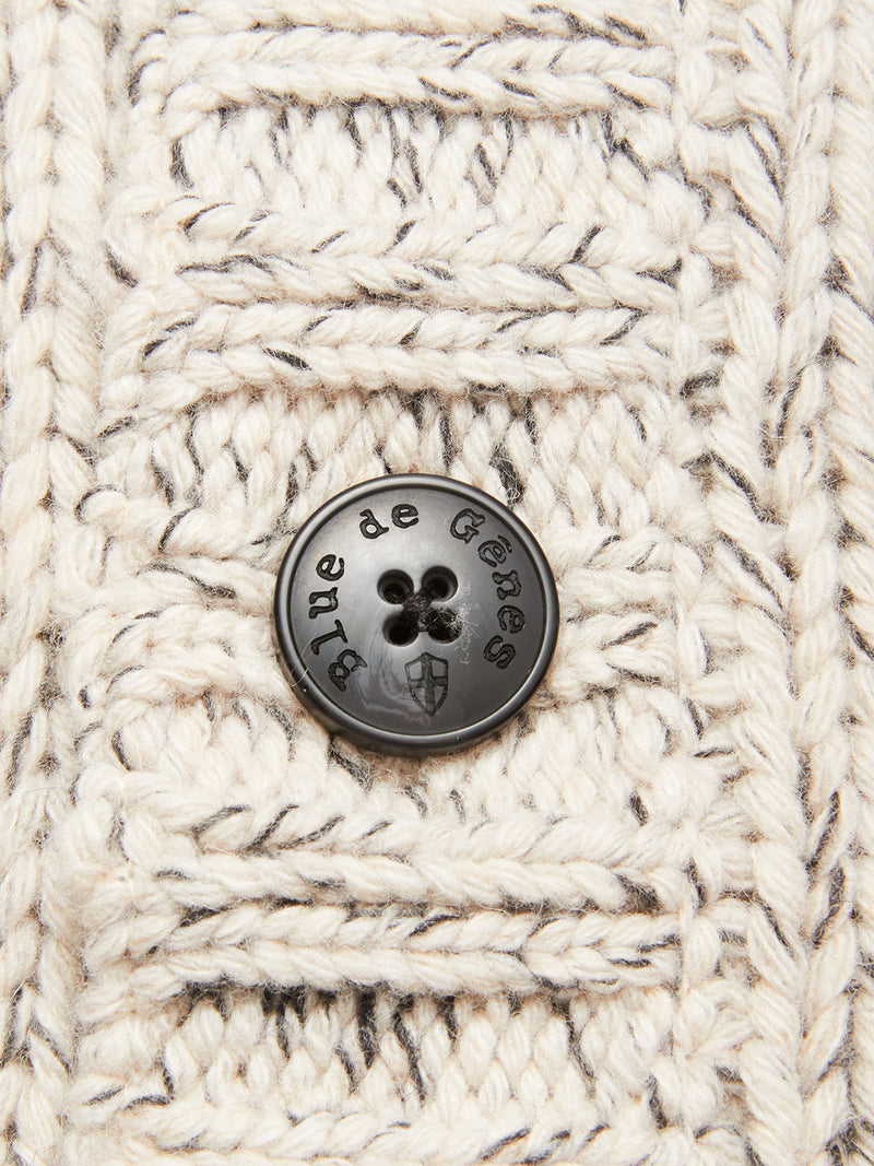 Close-up of the chunky knit cream and gray fabric from the Sakura Knit Cardigan - Stone by Blue de Gênes, showcasing a black button engraved with the brand name and a small shield emblem.