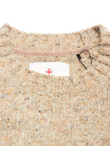 Close-up of the collar of the Blue de Gênes Honshu Crewneck Knit - Fungi, a beige speckled lambswool blend sweater with ribbed edges. A tag with a red cross shield is partly visible inside the neckline, plus a black plastic fastener.