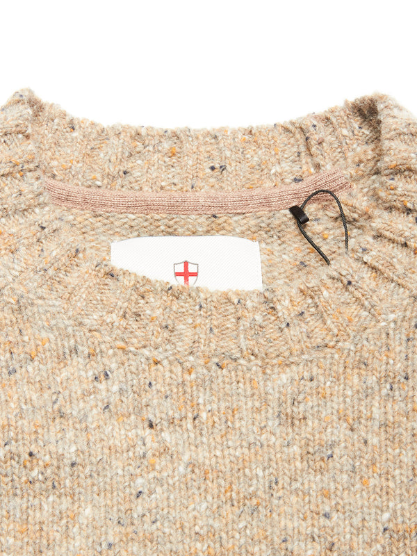 Close-up of the collar of the Blue de Gênes Honshu Crewneck Knit - Fungi, a beige speckled lambswool blend sweater with ribbed edges. A tag with a red cross shield is partly visible inside the neckline, plus a black plastic fastener.