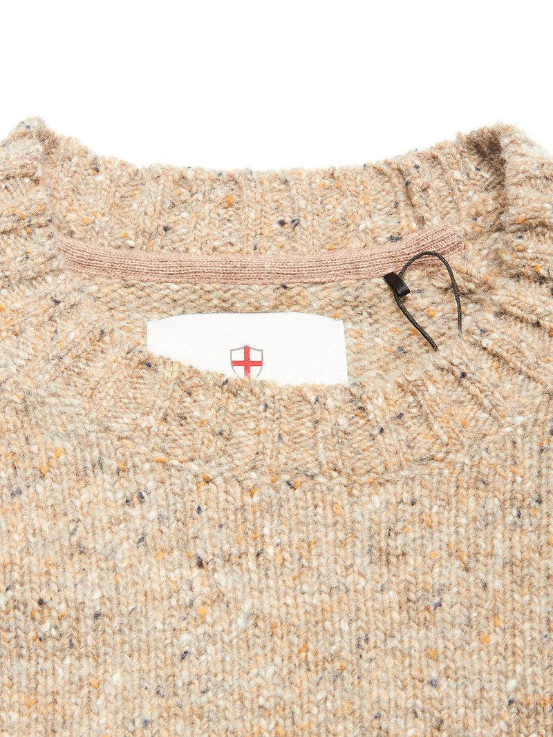 Close-up of the collar of the Blue de Gênes Honshu Crewneck Knit - Fungi, a beige speckled lambswool blend sweater with ribbed edges. A tag with a red cross shield is partly visible inside the neckline, plus a black plastic fastener.