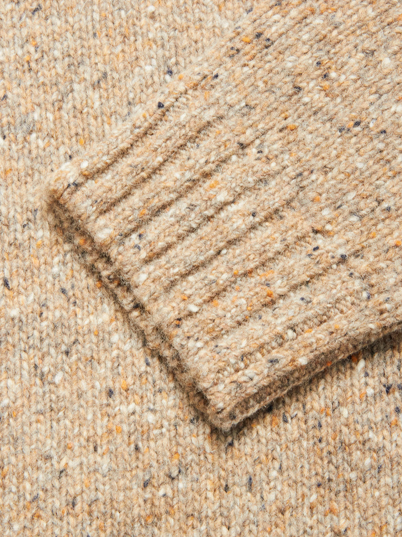 Close-up of the Blue de Gênes Honshu Crewneck Knit - Fungi sleeve, featuring a beige speckled lambswool blend with ribbed cuff and textured flecks of orange, brown, and dark blue on a light background.