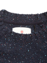 A close-up of the collar on the Blue de Gênes Honshu Crewneck Knit in navy, featuring chunky multicolored speckled knit and a white tag with a red cross shield logo inside the neckline.