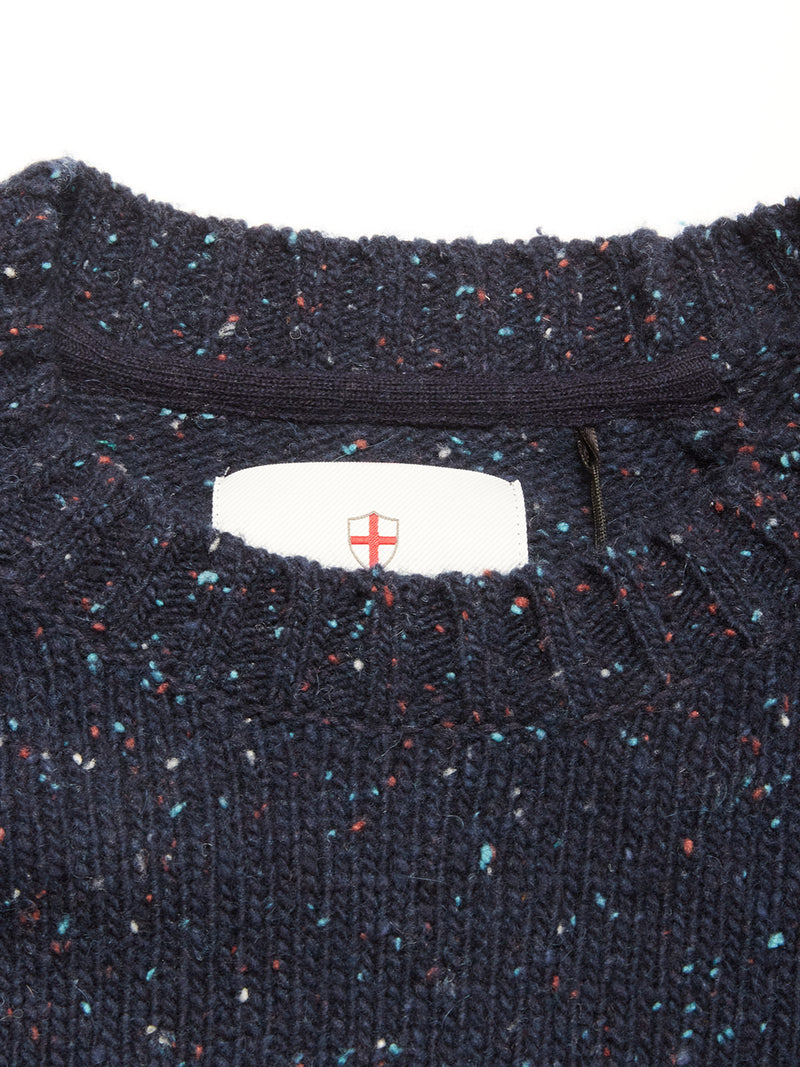 A close-up of the collar on the Blue de Gênes Honshu Crewneck Knit in navy, featuring chunky multicolored speckled knit and a white tag with a red cross shield logo inside the neckline.