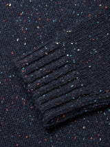 A close-up of the Blue de Gênes Honshu Crewneck Knit in navy, featuring colorful red, white, and blue speckles. The image highlights a ribbed cuff atop the cozy lambswool blend sweater.