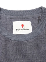 Close-up of the neckline on the Porto Knit - Dark Slate sweater by Blue de Gênes, featuring textured blue knit, a crewneck design, and a white label with Blue de Gênes branding and a red-and-white shield logo.