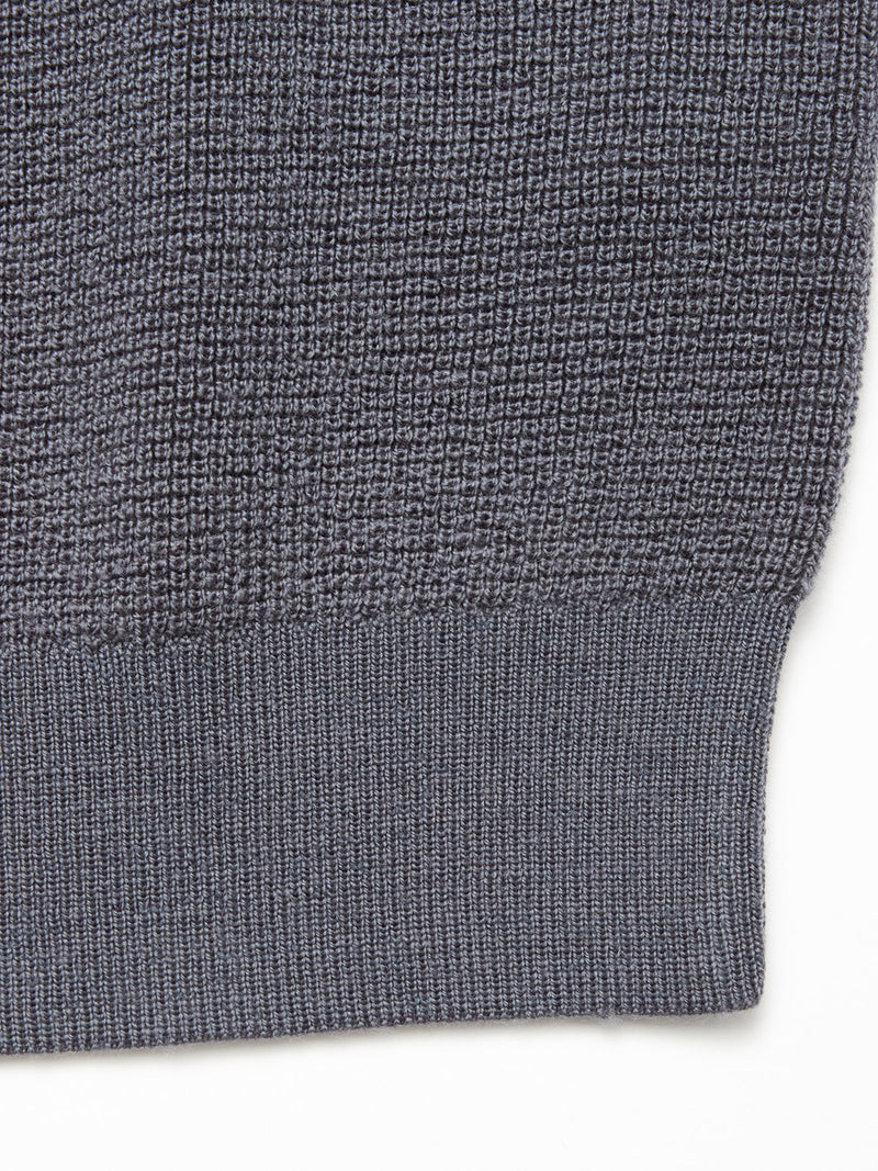 Close-up of the Porto Knit - Dark Slate by Blue de Gênes, featuring textured dark gray 100% wool fabric with a ribbed hem and transition to a waffle pattern, typical in this men's crewneck sweater.