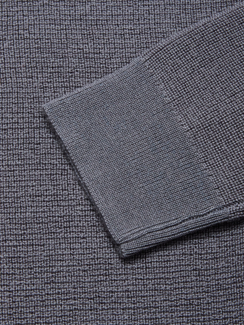 A close-up of the Porto Knit - Dark Slate sweater by Blue de Gênes, showcasing its textured 100% wool crewneck design with a neatly folded cuff and contrasting weave—an essential detail in refined menswear.