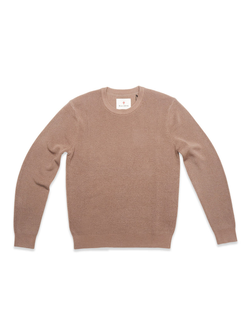 The Porto Knit - Fungi by Blue de Gênes is a light brown, long-sleeve crewneck sweater in 100% wool with a classic design and ribbed cuffs and waistband, shown laid flat on a white background.
