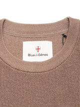 Close-up of the Blue de Gênes Porto Knit - Fungi: a brown textured 100% wool crewneck sweater with a sewn-in white label featuring a red shield—an elevated staple in menswear.