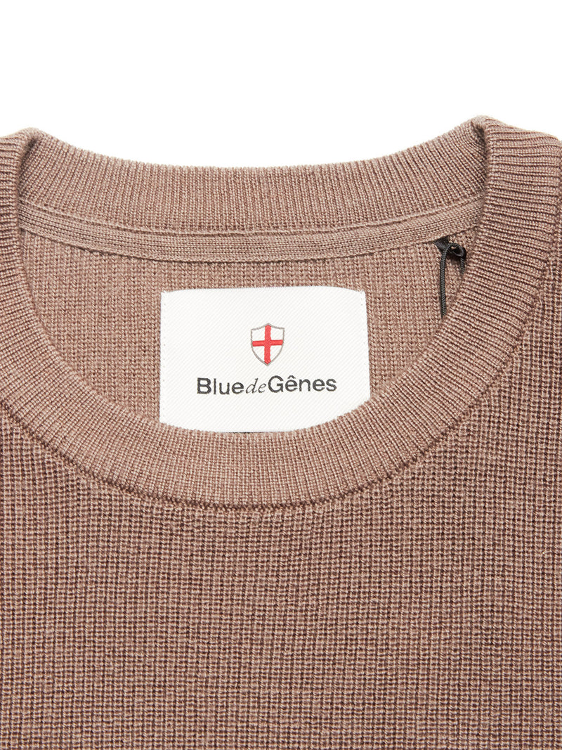 Close-up of the Blue de Gênes Porto Knit - Fungi: a brown textured 100% wool crewneck sweater with a sewn-in white label featuring a red shield—an elevated staple in menswear.