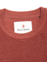 Close-up of the Porto Knit - Henna crewneck sweater by Blue de Gênes, featuring a white brand label and red and white shield emblem—a refined piece for any menswear collection.