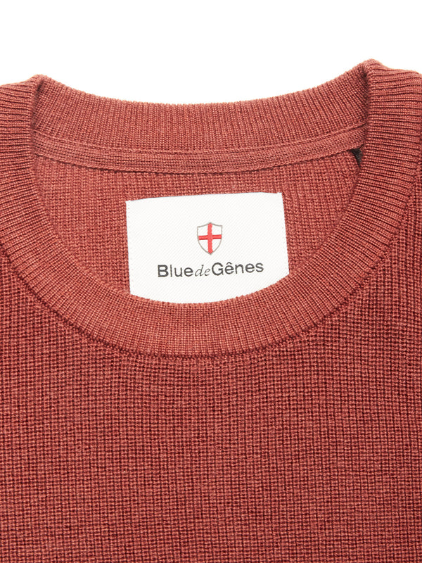 Close-up of the Porto Knit - Henna crewneck sweater by Blue de Gênes, featuring a white brand label and red and white shield emblem—a refined piece for any menswear collection.