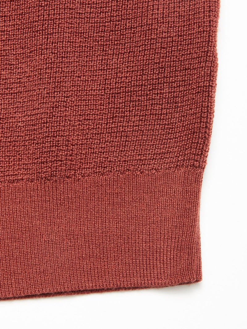 A close-up of the Blue de Gênes Porto Knit - Henna highlights its ribbed hem and textured knit detail along the bottom edge against a white background.