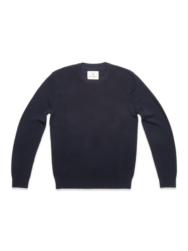 The Blue de Gênes Porto Knit in navy is a classic men's wool crewneck sweater, shown laid flat on a white background with a small white tag at the neckline.