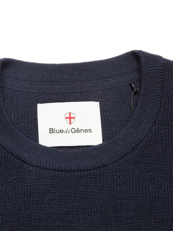 Close-up of the Porto Knit - Navy crewneck sweater by Blue de Gênes, featuring a white label with the brand name and red shield logo inside the collar—a stylish addition to your menswear collection.