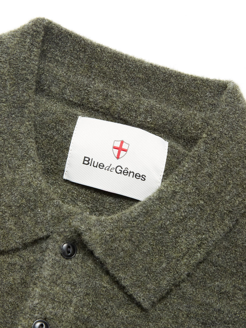 Close-up of the textured collar and corozo buttons on the Malakka Polo Knit - Army by Blue de Gênes. The inside label displays Blue de Gênes with a red cross emblem on a white background.