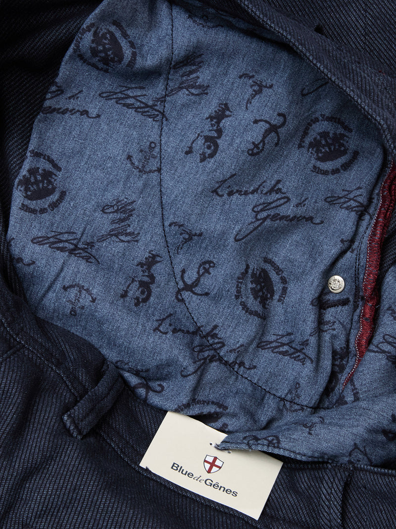 Close-up of the inner waistband of navy Menzo Olanda Chino pants by Blue de Gênes, featuring a blue fabric lining with dark script-style writing and symbols. The Blue de Gênes tag with a red and white shield appears at the bottom.