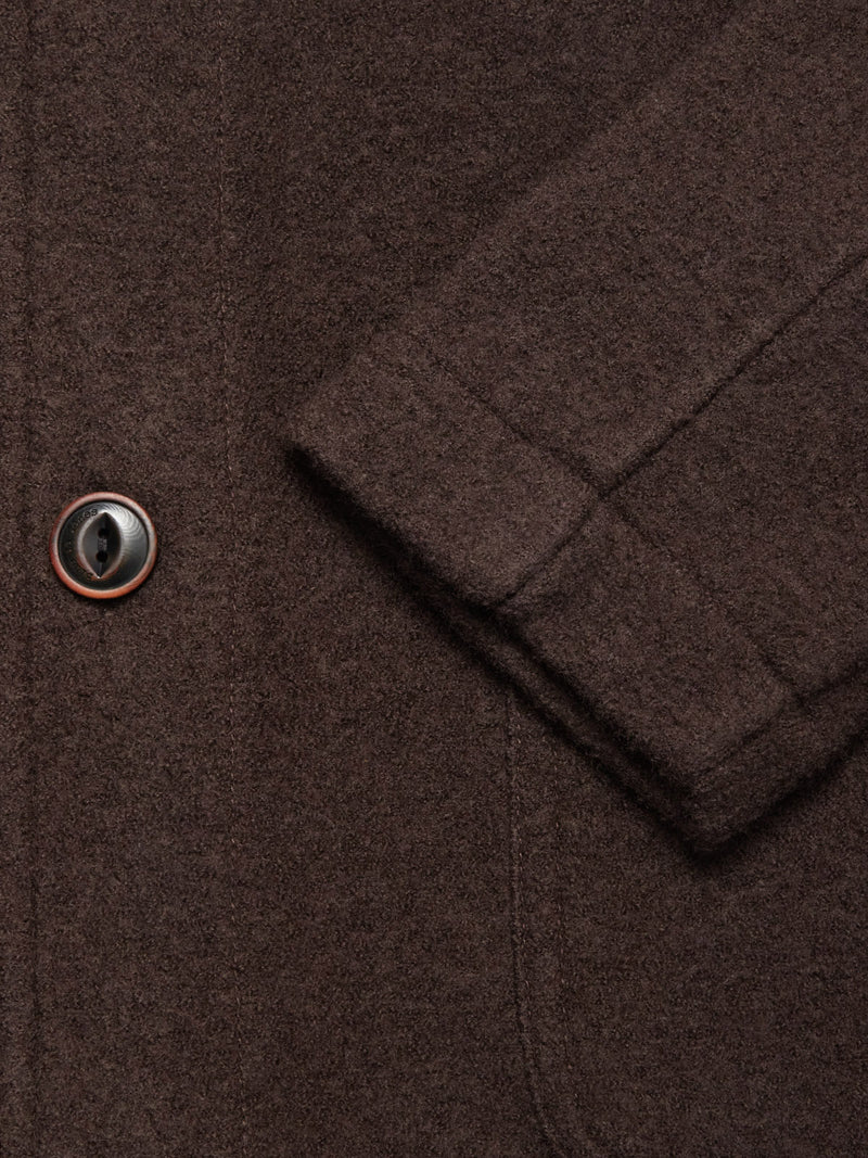 Close-up of the Blue de Gênes Kojima Wool Jacket - Chocolate, highlighting its textured brown boiled wool, a black and brown button, visible stitching, pocket seam, and part of the sleeve for a classic look.
