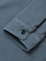 A close-up of a Blue de Gênes Nagano Overshirt - Dark Slate cuff with a black button, showcasing the garment dyed cotton Moleskin fabric texture and detailed stitching.