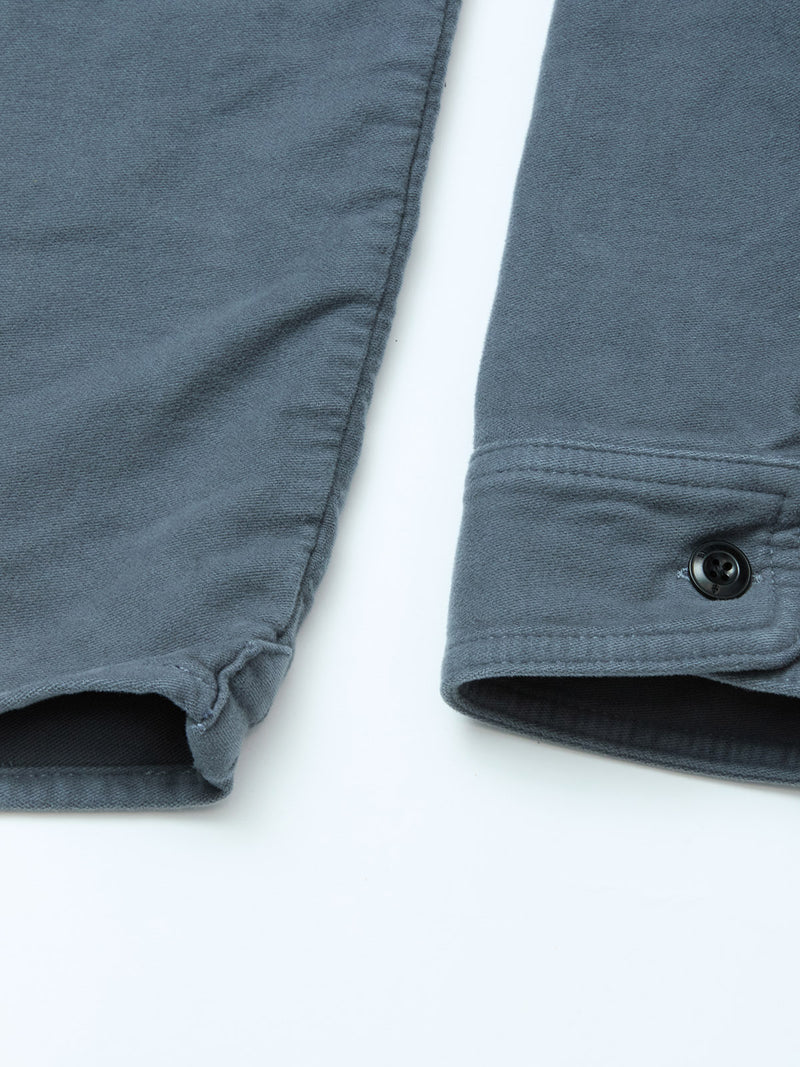 Close-up of the cuffs on a Blue de Gênes Nagano Overshirt - Dark Slate in cotton moleskin, with a black button, visible stitching, and soft fabric against a light background.