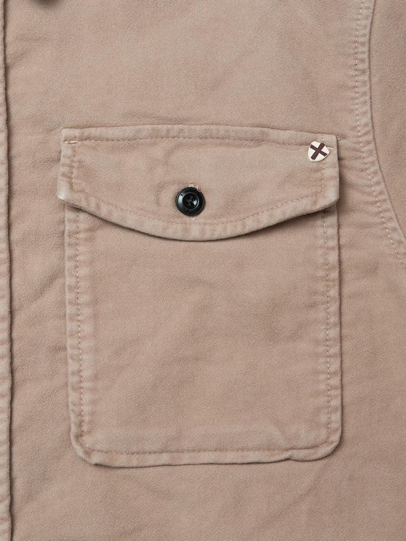 Close-up of the Nagano Overshirt - Fungi by Blue de Gênes featuring a beige cotton moleskin pocket with flap, black button closure, and a small stitched X detail in dark thread on the upper right corner.