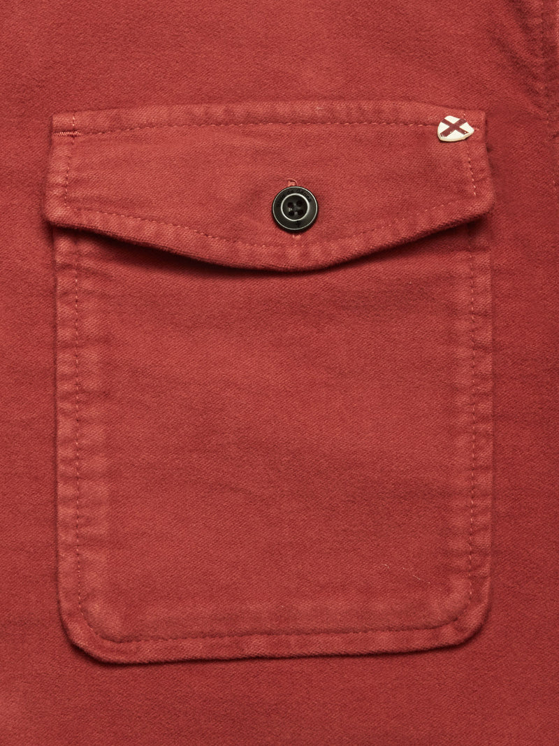 Close-up of the pocket on the Blue de Gênes Nagano Overshirt in Henna, featuring rust-colored moleskin cotton, a buttoned flap, and a small stitched white detail on the upper right corner of the flap.