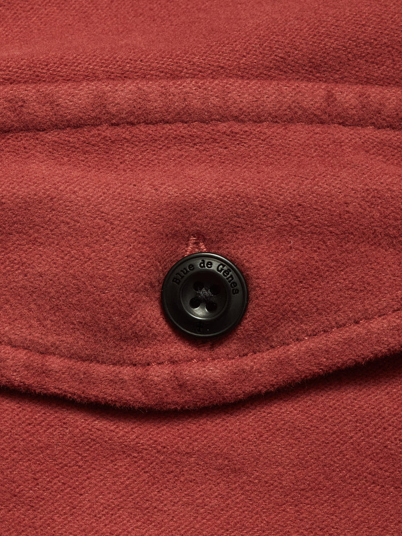Close-up of the Blue de Gênes Nagano Overshirt in Henna, featuring red garment-dyed Moleskin cotton, a flap detail, and a black button engraved with the brand name.