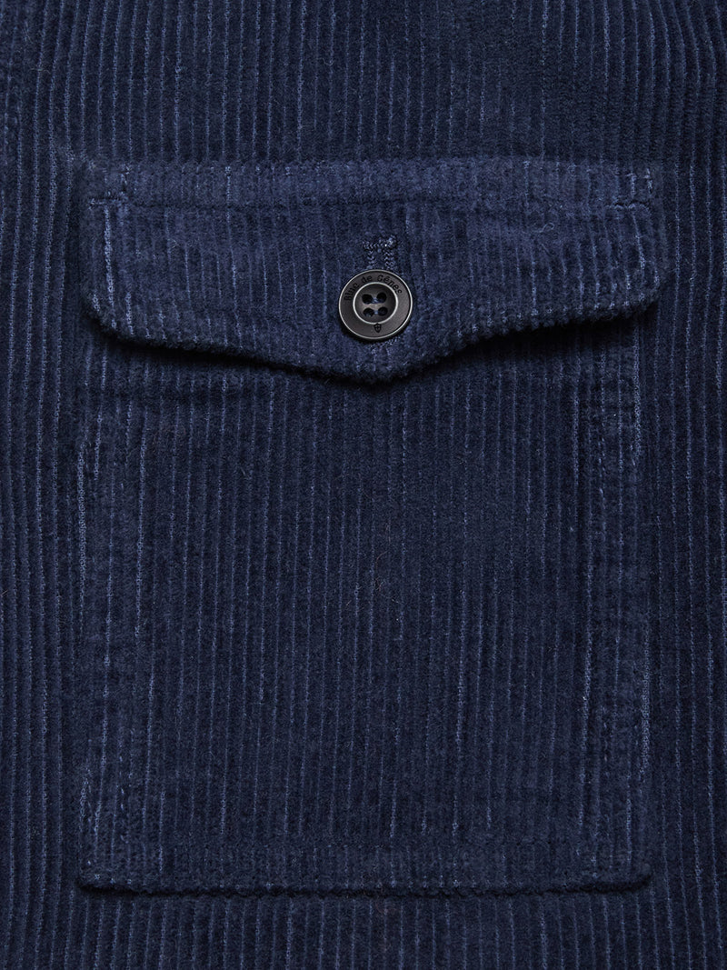 Close-up of the Blue de Gênes Masami Cord Blazer - Navy, garment dyed for rich color. Its corduroy fabric has vertical ridges, a patch pocket with flap and black button, emphasizing this stylish textured piece.