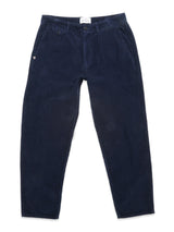 The Blue de Gênes Etsu Cord Chino in navy is a pair of garment-dyed, relaxed fit corduroy trousers with button and zip closure, slanted front pockets, and a logo patch on the left pocket, shown laid flat on white.