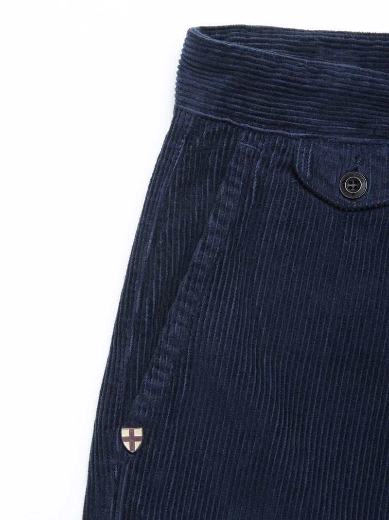 Close-up of Blue de Gênes Etsu Cord Chino - Navy, showing a front pocket with a shield-shaped patch, buttoned waistband, relaxed fit, and visible ribbed texture.