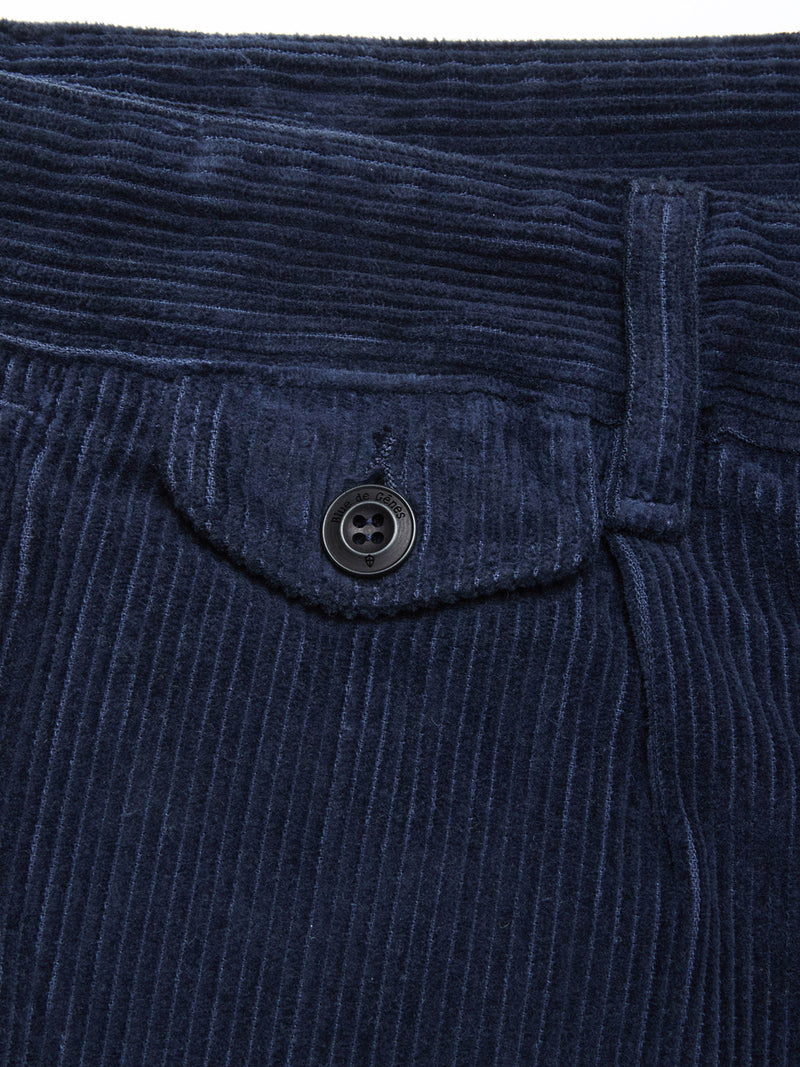 Close-up of Blue de Gênes Etsu Cord Chino - Navy, highlighting the waistband, belt loop, and small flap pocket with a black button. The relaxed fit and textured vertical corduroy ridges are clearly visible.