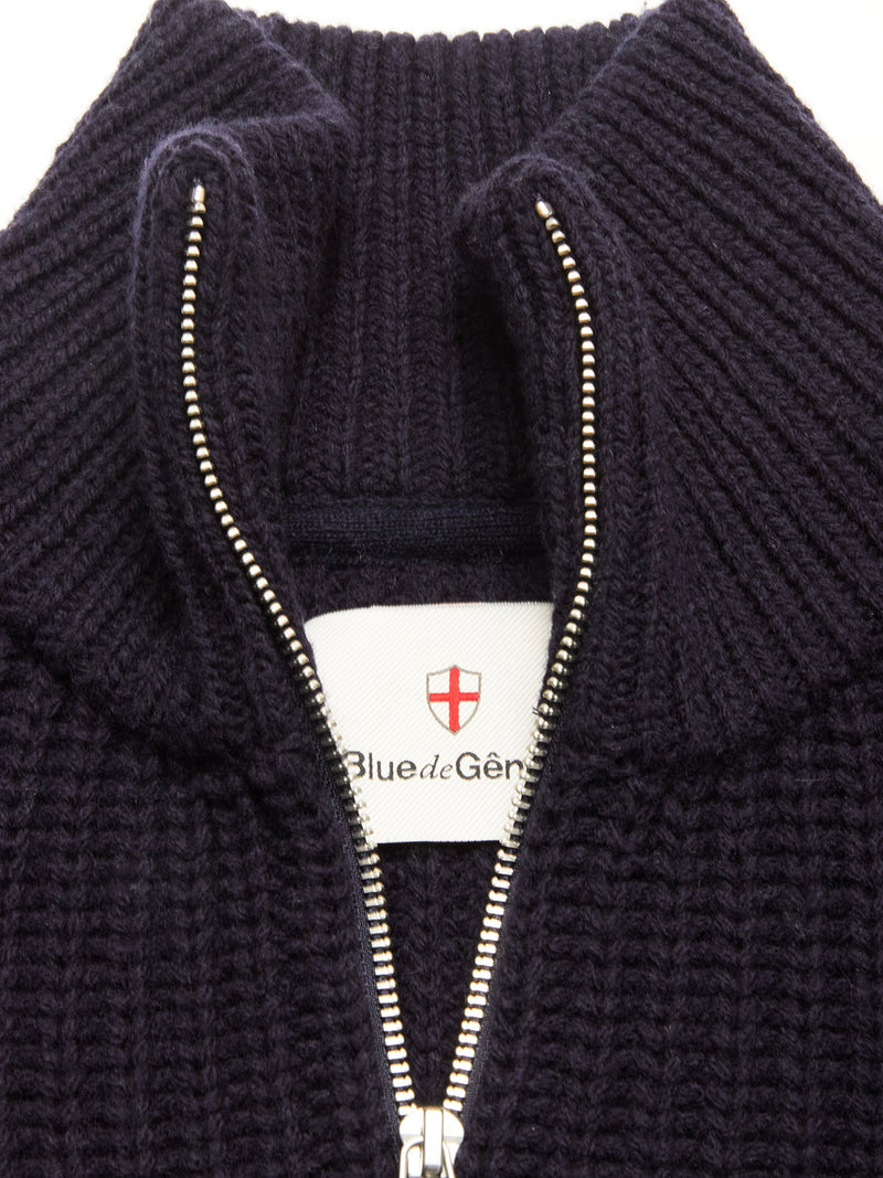 Close-up of the Yomaha Halfzip Knit in navy by Blue de Gênes, featuring a chunky knit, silver half-zip, exposed white brand label with red cross emblem—crafted from a premium wool blend for comfort and style.
