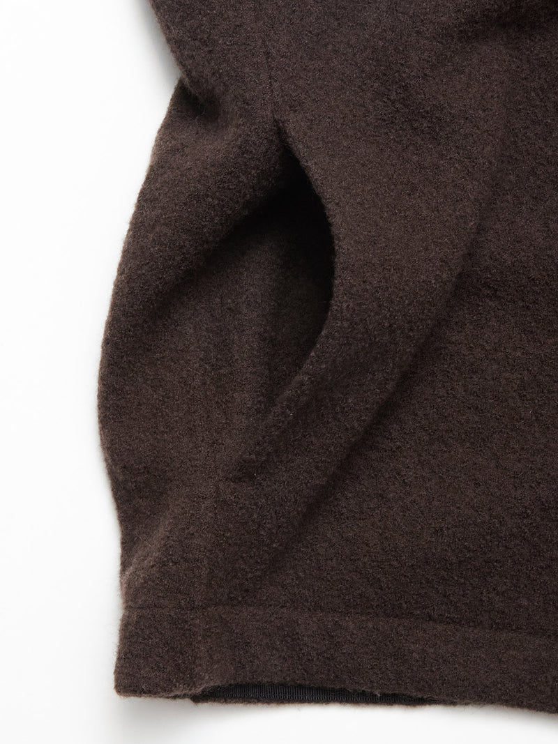 Close-up of the Blue de Gênes Koi Wool Gilet in Chocolate, showing its brown textured wool fabric with visible seams and a curved edge against a white background. The material appears soft, thick, and high-quality.