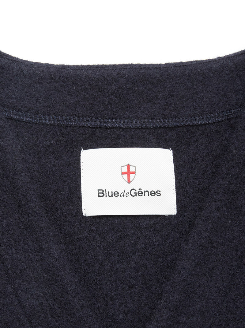 Close-up of the Koi Wool Gilet - Navy by Blue de Gênes, featuring a classic design with a dark blue boiled wool fabric and a white label under the brand's red and white shield logo.