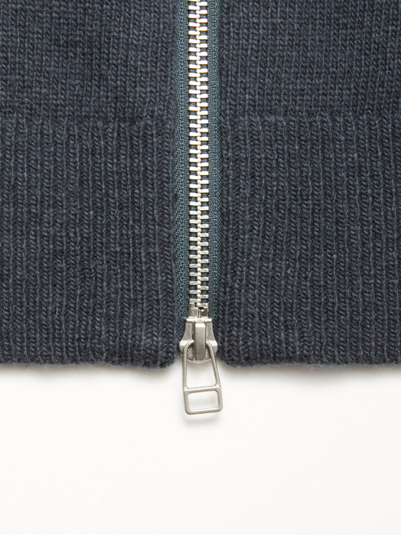 Close-up of a silver zipper partially unzipped on the thick, dark slate Nuvali Polo Cardigan by Blue de Gênes, shown against a white background.