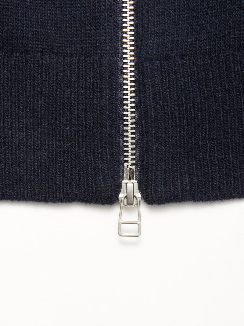 Close-up of the silver zipper on the Blue de Gênes Nuvali Polo Cardigan in Navy, partially unzipped on ribbed knit fabric, with the slider and pull tab centered at the bottom.