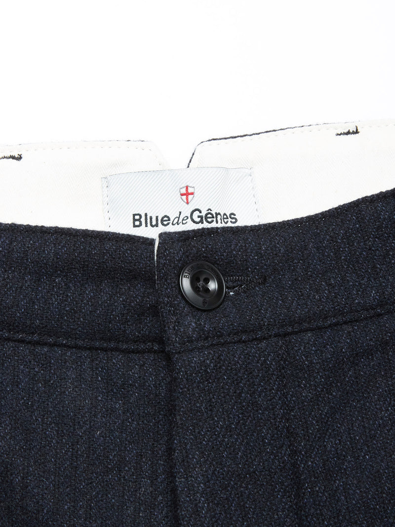 Close-up of the waistband of the Blue de Gênes Kibishi Solid Pant in dark navy, made from an Italian wool blend, with a black button and a white Blue de Gênes label beneath a small red and white shield emblem.