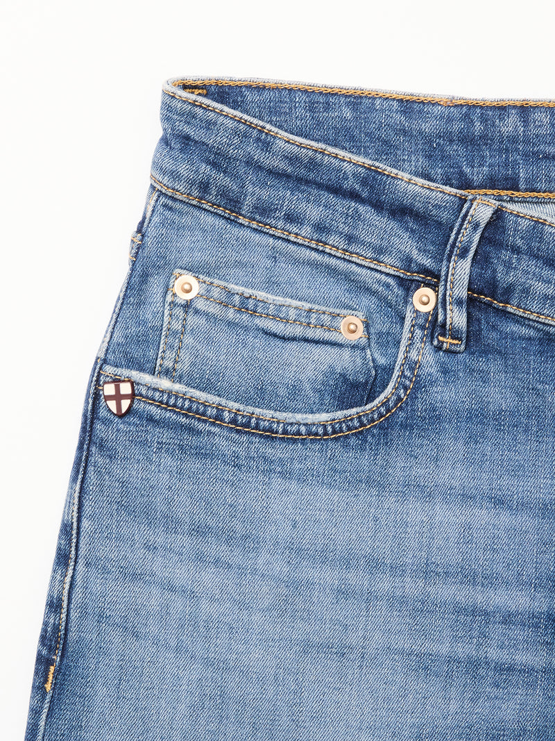 Close-up of the front pocket on Vinci Girisha Used Jeans by Blue de Gênes, highlighting stitching, a riveted coin pocket, and a shield-shaped patch with a red cross on white at the edge of this classic five-pocket style.