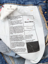 Close-up of the inside of Blue de Gênes Vinci Girisha Used Jeans, showing a white label with brand and product name, a printed Leonardo da Vinci story, care labels, and yellow stitching on blue comfort stretch denim.