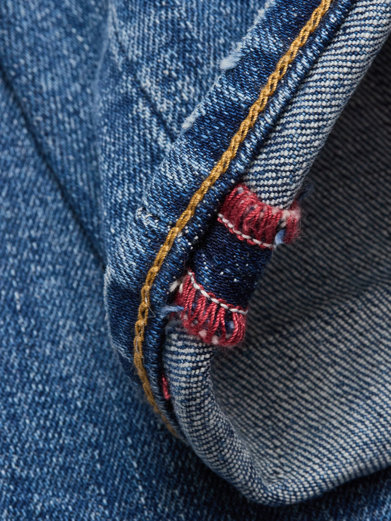 Close-up of the hem of Vinci Girisha Used Jeans by Blue de Gênes, featuring blue denim, detailed stitching, a yellow seam line, and red and white selvedge edge.