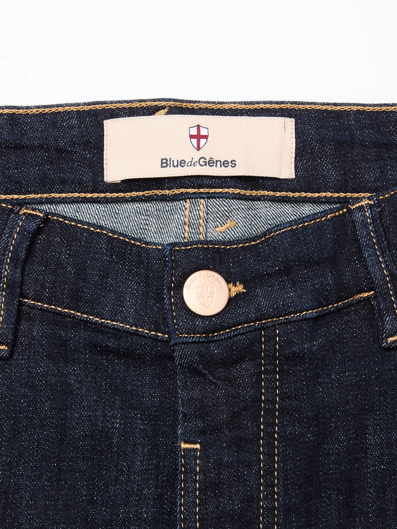 Close-up of the waistband on Blue de Gênes Vinci Girisha Rinse Jeans in rinse wash, showing comfort stretch dark blue denim, a metal button, and a sewn Blue de Gênes label below the red and white shield logo.