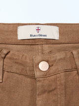 Close-up of the Vinci Iro Pant - Chocolate by Blue de Gênes, showing the comfort stretch waistband with a metal button embossed with a shield and a white label featuring a red cross and Blue de Gênes text.