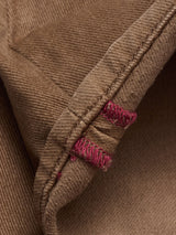 Close-up of the Vinci Iro Pant - Chocolate by Blue de Gênes, showing brown fabric with visible stitching and two buttonholes reinforced in pink thread. The texture and weave are inspired by regular fit jeans.