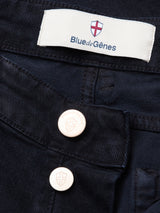 Close-up of Vinci Iro Pant in navy by Blue de Gênes, featuring two metallic shield-logo buttons and a white label under a red and white cross emblem, crafted from comfort stretch twill for all-day ease.