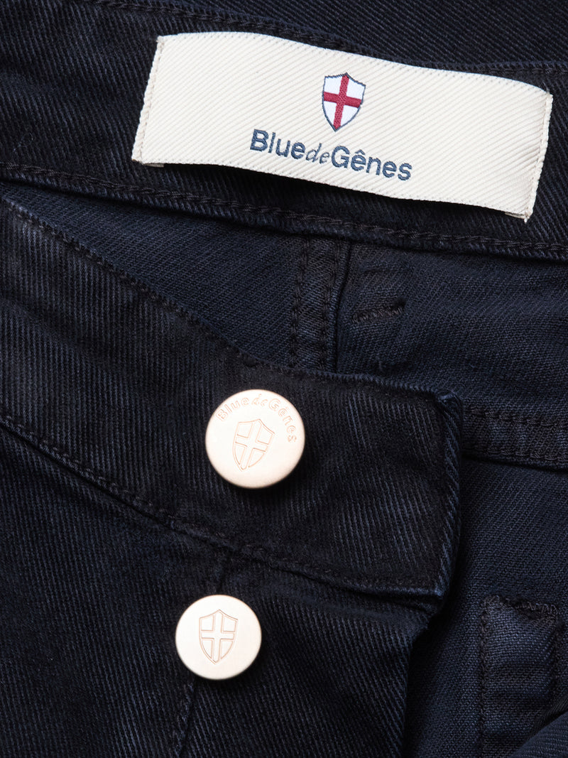 Close-up of Vinci Iro Pant in navy by Blue de Gênes, featuring two metallic shield-logo buttons and a white label under a red and white cross emblem, crafted from comfort stretch twill for all-day ease.
