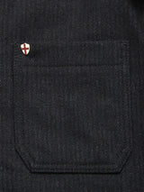 Close-up of a dark denim pocket with a small pin, alongside the Blue de Gênes Vincenzo Solid Jacket - Dark Navy, featuring a distinctive white shield design with red cross.