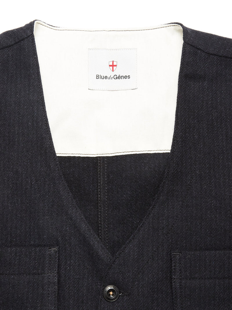 Close-up of the Maurice Solid Gilet - Dark Navy by Blue de Gênes, a refined Italian wool blend gilet with V-neckline, button closure, front pockets, and signature shield logo on the label.