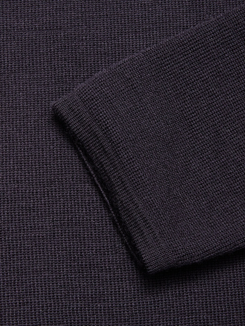 Close-up of the Toyama Knit L/S sweater by Blue de Gênes in dark navy, highlighting its textured waffle-knit pattern and folded edge lying at an angle on matching fabric.