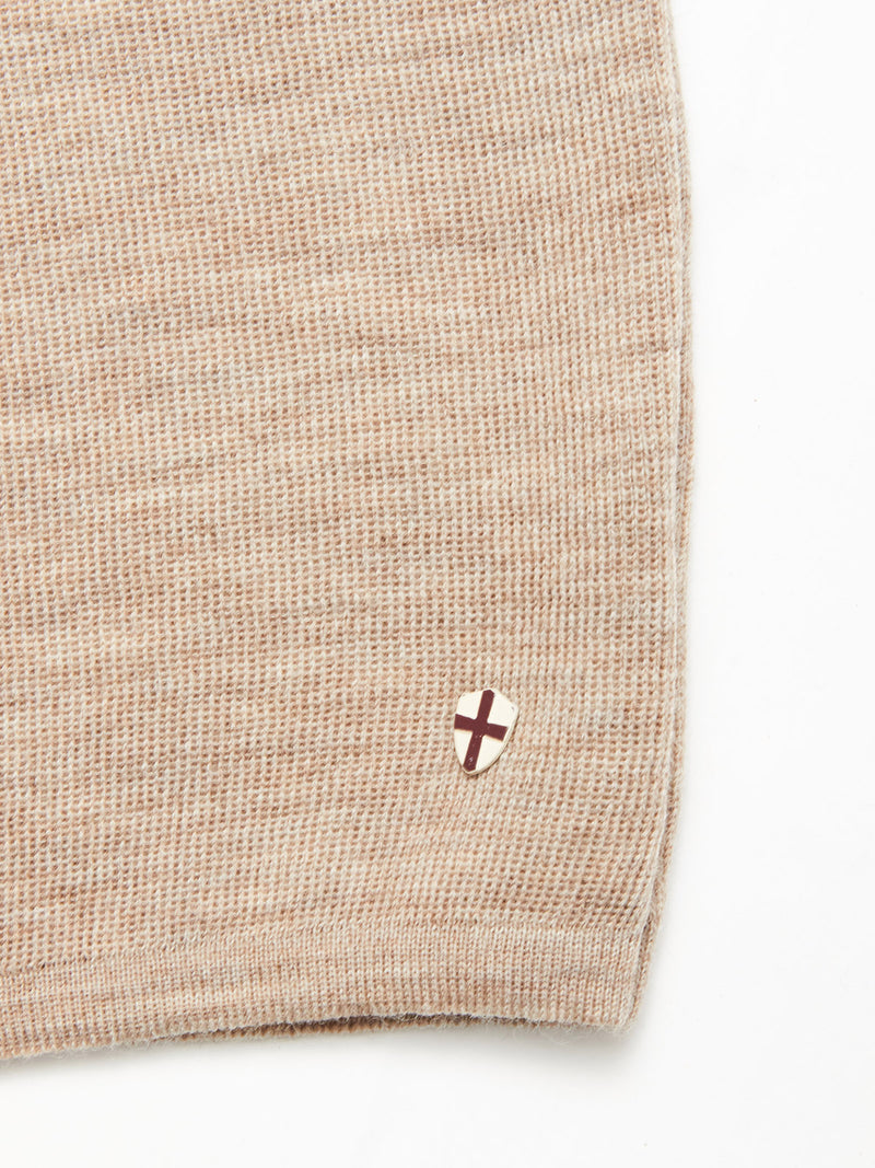 Close-up of the Blue de Gênes Toyama Knit L/S in oat, featuring textured beige Merino wool and a small shield patch near the edge with a maroon cross on a white background.