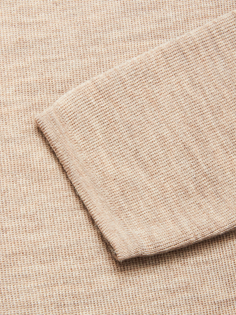 A close-up of the Blue de Gênes Toyama Knit L/S in Oat shows its beige Merino wool sleeve laid flat on a matching knit, highlighting the fabric’s detailed texture and stitching.
